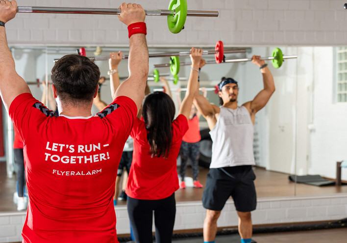 Gruppe in rotem Shirt hebt Hanteln bei Sportkurs im Fitnessraum